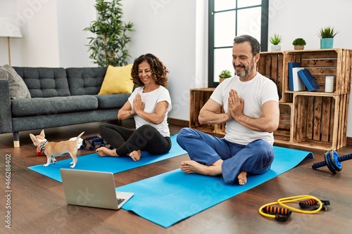 Middle age hispanic couple smiling happy doing online yoga class at home.