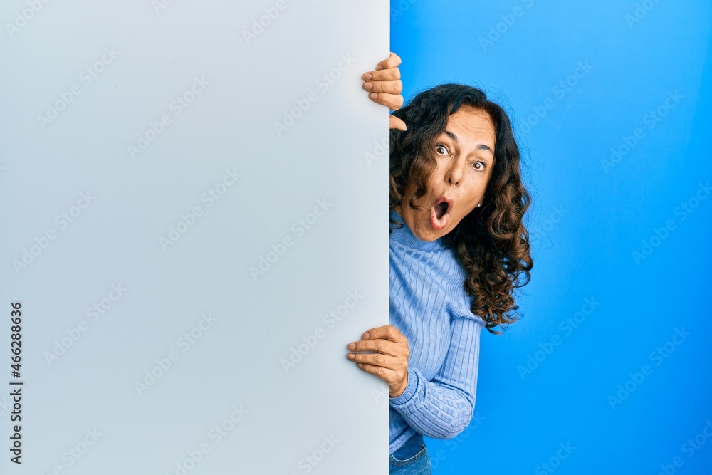 Middle age hispanic woman holding blank empty banner scared and amazed with open mouth for surprise, disbelief face Middle age hispanic woman holding blank empty banner scared and amazed with open mouth for surprise, disbelief face