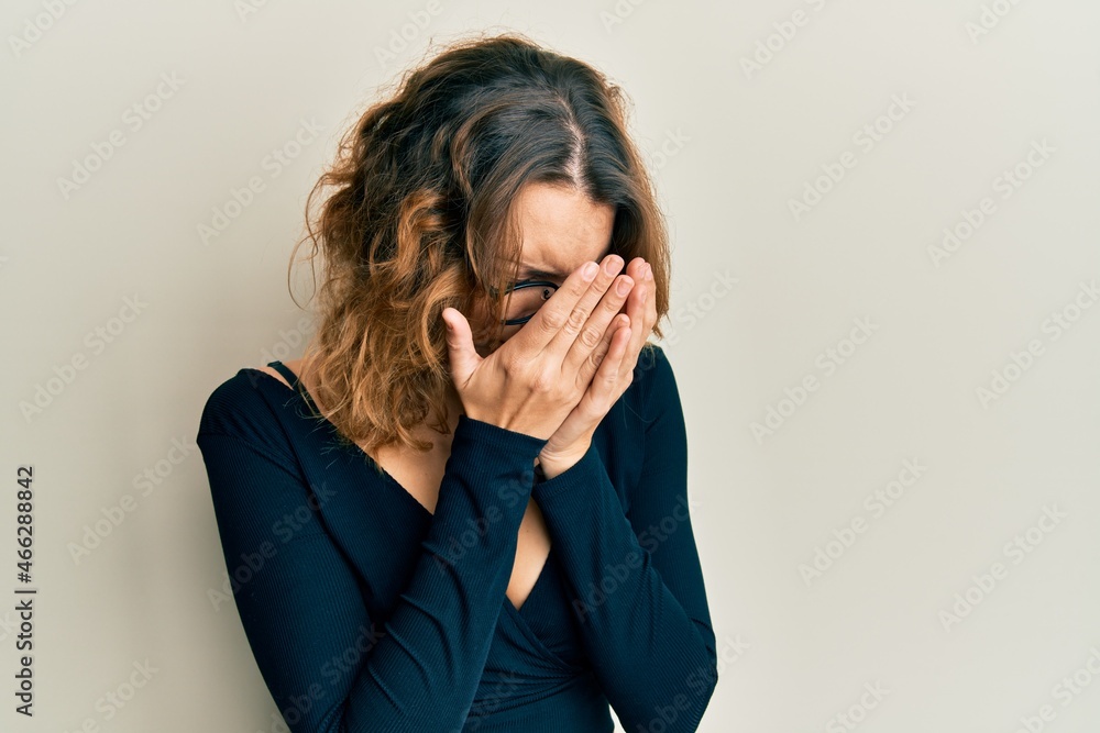 Young caucasian woman wearing business shirt and glasses with sad expression covering face with hands while crying. depression concept. Young caucasian woman wearing business shirt and glasses with sad expression covering face with hands while crying. depression concept.