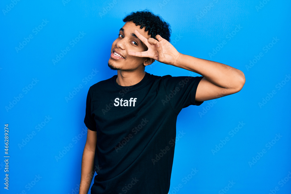 Young african american man wearing staff t shirt doing peace symbol with fingers over face, smiling cheerful showing victory Young african american man wearing staff t shirt doing peace symbol with fingers over face, smiling cheerful showing victory