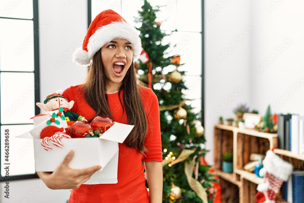Young brunette woman standing by christmas tree holding decoration angry and mad screaming frustrated and furious, shouting with anger. rage and aggressive concept. Young brunette woman standing by christmas tree holding decoration angry and mad screaming frustrated and furious, shouting with anger. rage and aggressive concept.