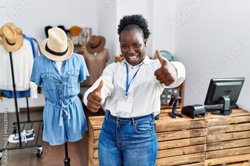 Young african woman working as manager at retail boutique approving doing positive gesture with hand, thumbs up smiling and happy for success. winner gesture.