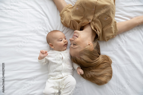 Top view loving young mother and baby lying on bed white sheet, happy caring mom with little first child, newborn kid relaxing spending leisure time together, motherhood and childhood concept