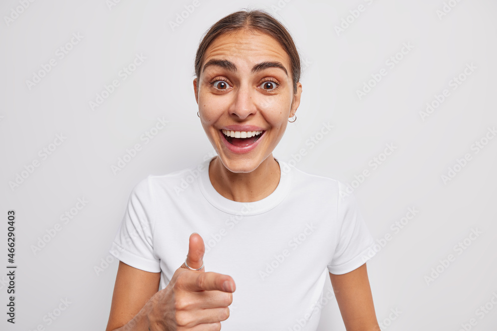 Happy young woman looks with surprised cheerful expression smiles toothily indicatesindex finger at you wears casual t shirt isolated over white background notices something very funny forward Happy young woman looks with surprised cheerful expression smiles toothily indicatesindex finger at you wears casual t shirt isolated over white background notices something very funny forward