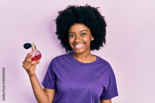 Young african american woman holding perfume looking positive and happy standing and smiling with a confident smile showing teeth