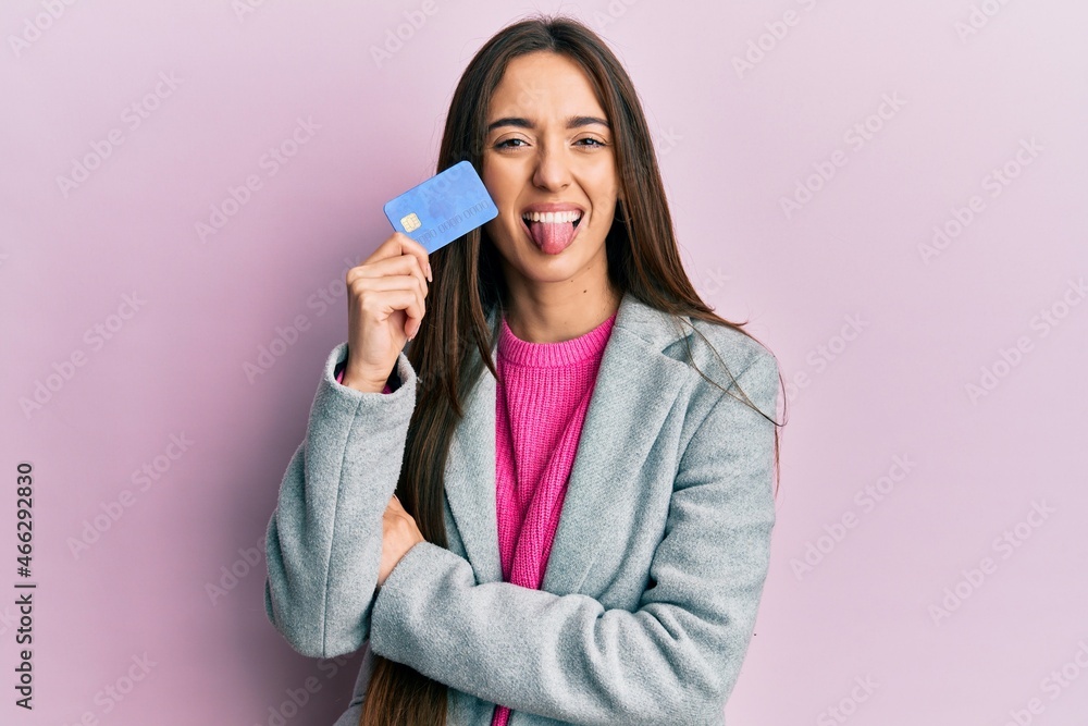 Young hispanic girl holding credit card sticking tongue out happy with funny expression. Young hispanic girl holding credit card sticking tongue out happy with funny expression.