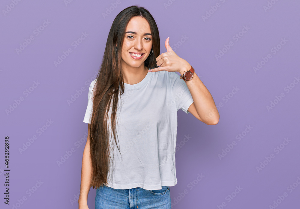 Young hispanic girl wearing casual white t shirt smiling doing phone gesture with hand and fingers like talking on the telephone. communicating concepts. Young hispanic girl wearing casual white t shirt smiling doing phone gesture with hand and fingers like talking on the telephone. communicating concepts.