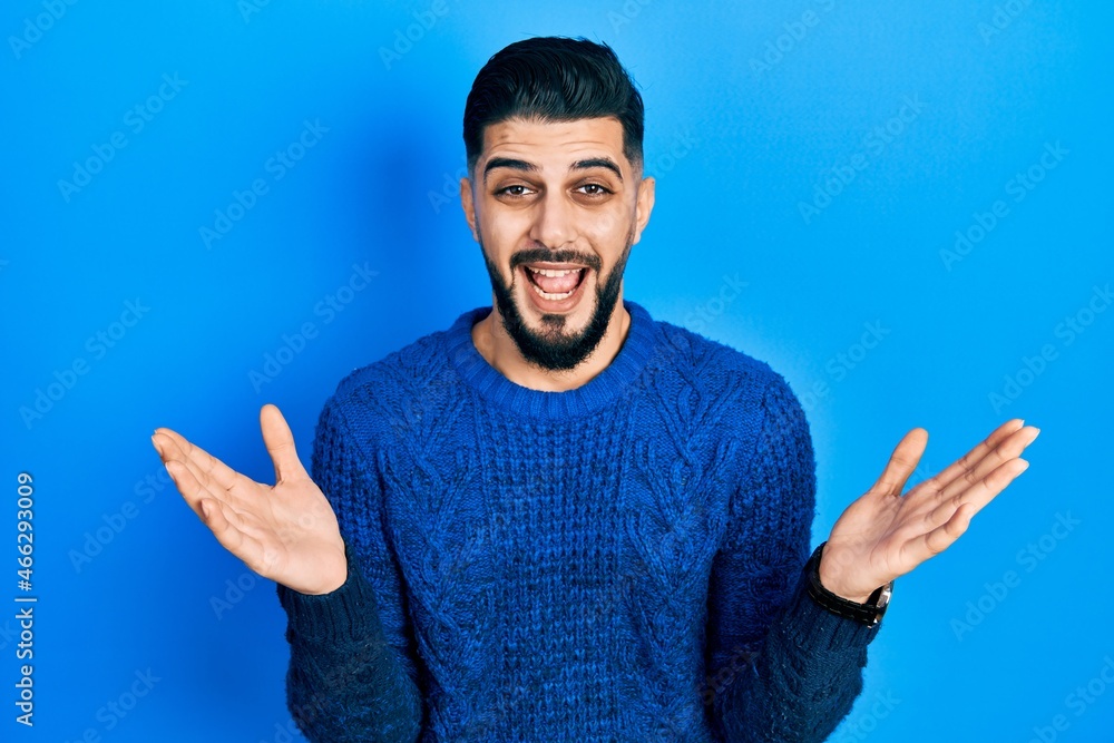 Handsome man with beard wearing casual winter sweater celebrating victory with happy smile and winner expression with raised hands Handsome man with beard wearing casual winter sweater celebrating victory with happy smile and winner expression with raised hands
