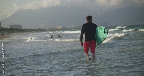 A retired athlete enters the sea, goes to ride on the waves on surfing dos. Portrait of a handsome senior sportsman at the age carrying a surfboard on the beach.