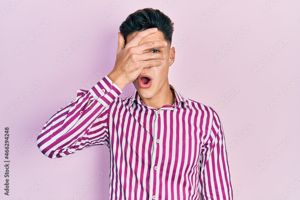 Young hispanic man wearing casual clothes peeking in shock covering face and eyes with hand, looking through fingers with embarrassed expression. Young hispanic man wearing casual clothes peeking in shock covering face and eyes with hand, looking through fingers with embarrassed expression.