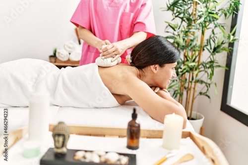 Middle age hispanic woman smiling confident having back massage using thai bags at beauty center
