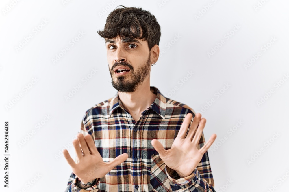 Hispanic man with beard standing over isolated background afraid and terrified with fear expression stop gesture with hands, shouting in shock. panic concept. Hispanic man with beard standing over isolated background afraid and terrified with fear expression stop gesture with hands, shouting in shock. panic concept.