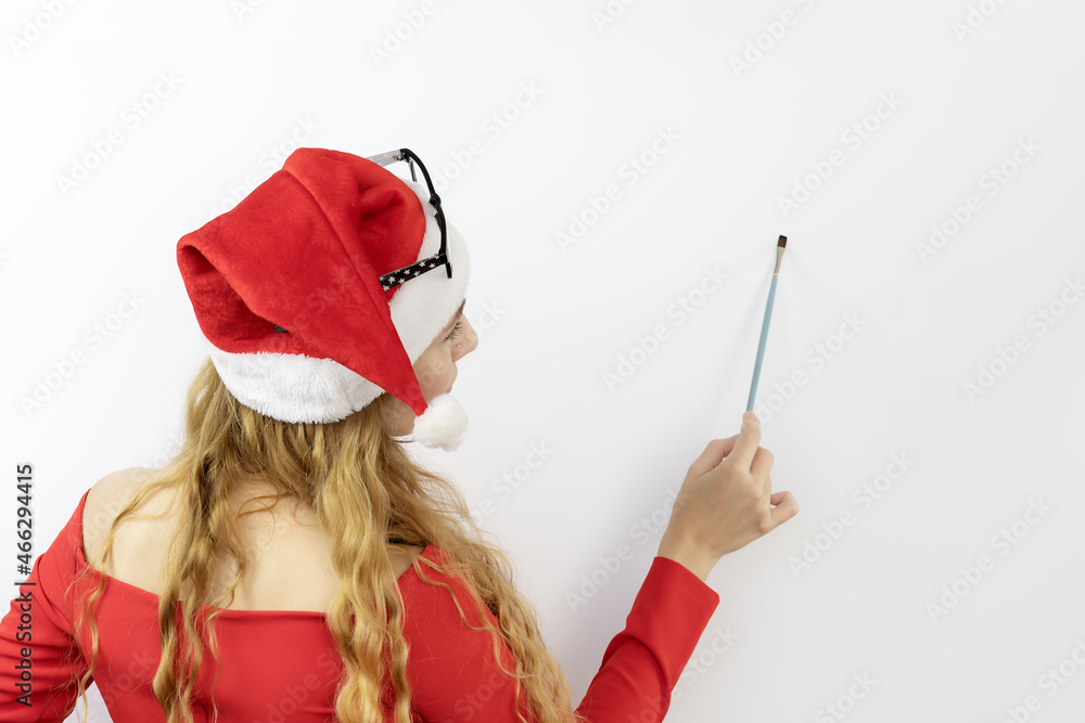 A girl in santa outfit risks a paintbrush on a white wall. Lady santa artist. Christmas mockup. A girl in santa outfit risks a paintbrush on a white wall. Lady santa artist. Christmas mockup.