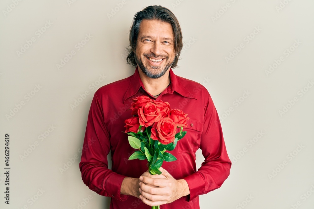 Middle age handsome man holding bouquet of red roses smiling and laughing hard out loud because funny crazy joke. Middle age handsome man holding bouquet of red roses smiling and laughing hard out loud because funny crazy joke.