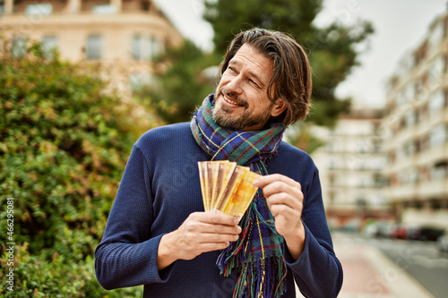 Middle age handsome man holding norwegian krone banknotes outdoors at the park