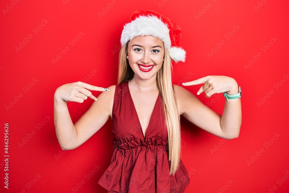 Young blonde girl wearing christmas hat looking confident with smile on face, pointing oneself with fingers proud and happy. Young blonde girl wearing christmas hat looking confident with smile on face, pointing oneself with fingers proud and happy.