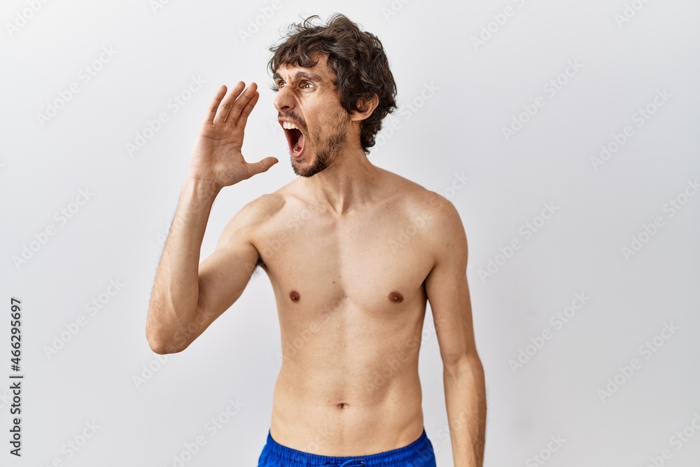Fototapeta premium Young hispanic man standing shirtless over isolated, background shouting and screaming loud to side with hand on mouth. communication concept.