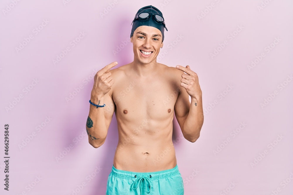 Young hispanic man wearing swimwear and swimmer glasses smiling cheerful showing and pointing with fingers teeth and mouth. dental health concept.