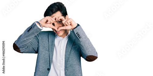 Young hispanic man wearing business clothes doing heart shape with hand and fingers smiling looking through sign