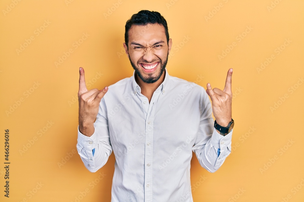 Hispanic man with beard wearing business shirt shouting with crazy expression doing rock symbol with hands up. music star. heavy concept.