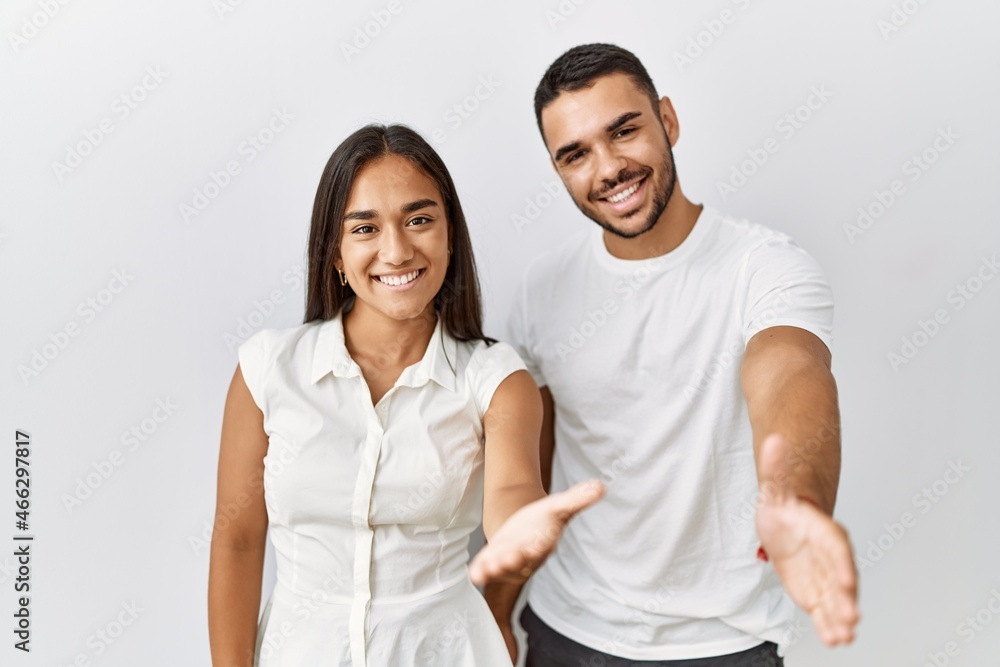 Young interracial couple standing together in love over isolated background smiling friendly offering handshake as greeting and welcoming. successful business. Young interracial couple standing together in love over isolated background smiling friendly offering handshake as greeting and welcoming. successful business.