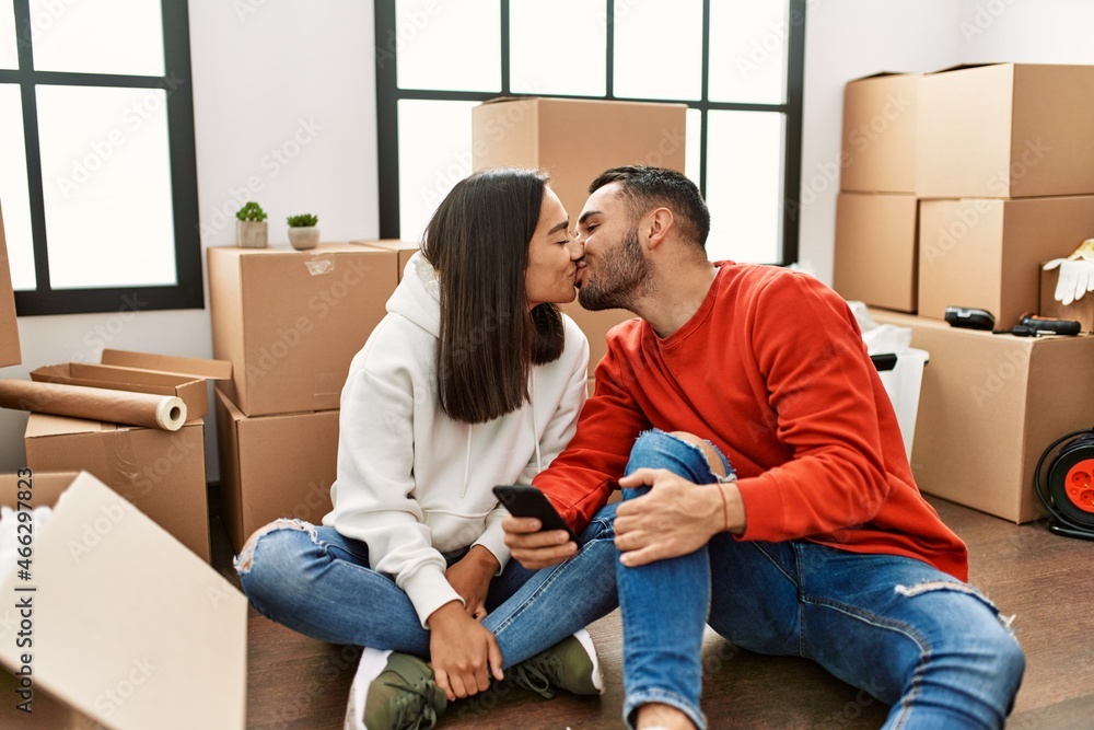 Young latin couple kissing and using smartphone at new home. Young latin couple kissing and using smartphone at new home.