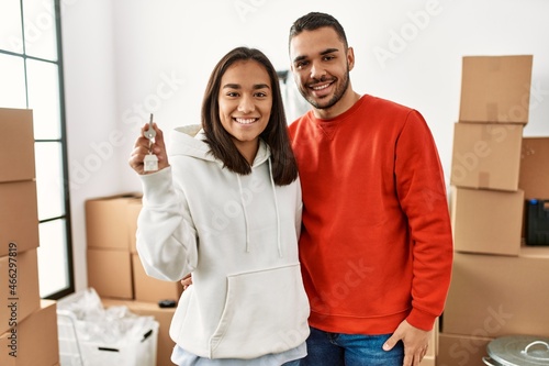 Young hispanic couple smiling happy holding key of new home.