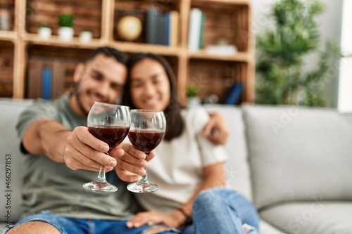 Young latin couple smiling happy toasting with red wine glass at home.