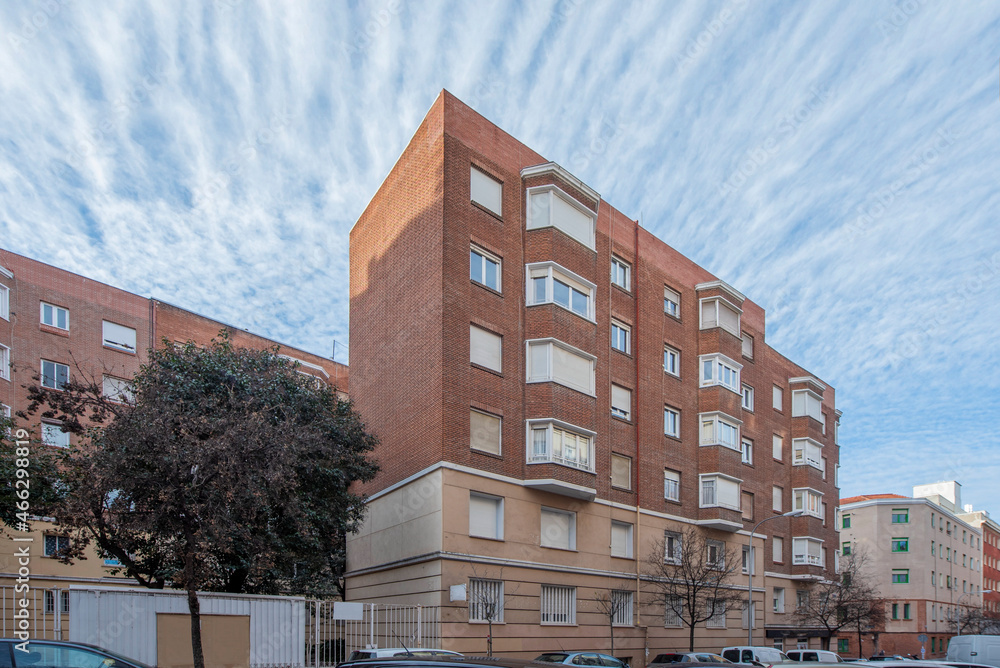 Red clay brick building facade with large windows on a winter day with deciduous trees and sky with wind blown cirrocumulus
