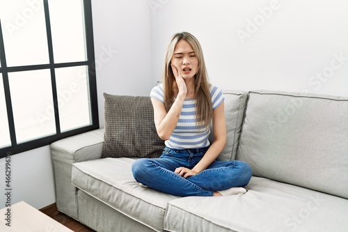 Asian young woman sitting on the sofa at home touching mouth with hand with painful expression because of toothache or dental illness on teeth. dentist