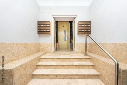 Entrance staircase to a residential home with an elevator with golden doors and marble stairs with ocher-colored aluminum mailboxes