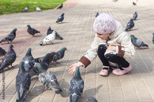 a girl in a white jacket feeds pigeons in the park in the spring