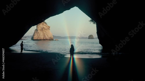 Aerial: Woman with light ray aura looking out of a cave. Cathedral cove, New Zealand photo