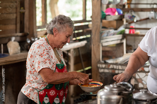 Mujer adulta mayor cocinando en una estufa metálica con leña en su casa de madera  photo