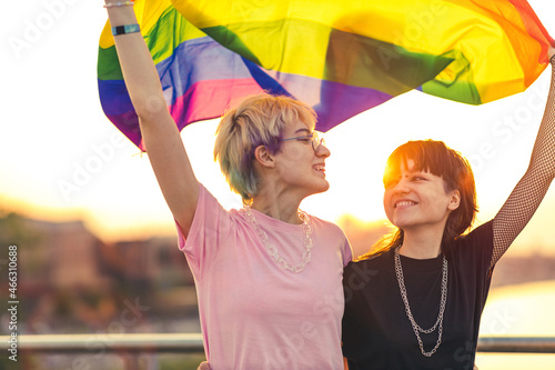 Portrait of happy non binary couple waving rainbow flag
