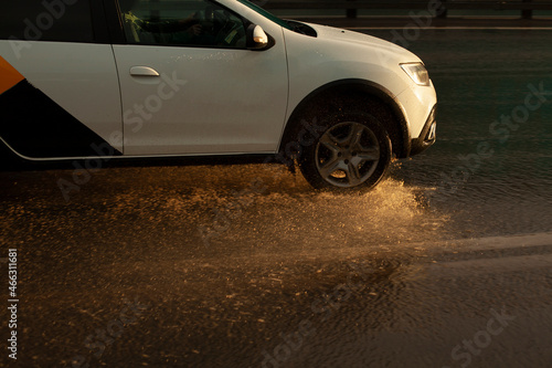 The car is driving in a puddle. Splashes of water from the wheels of the car. Transport on the highway.