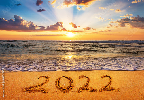 Happy New Year 2022 is coming concept. Number 2022 written on seashore sand at sunrise.