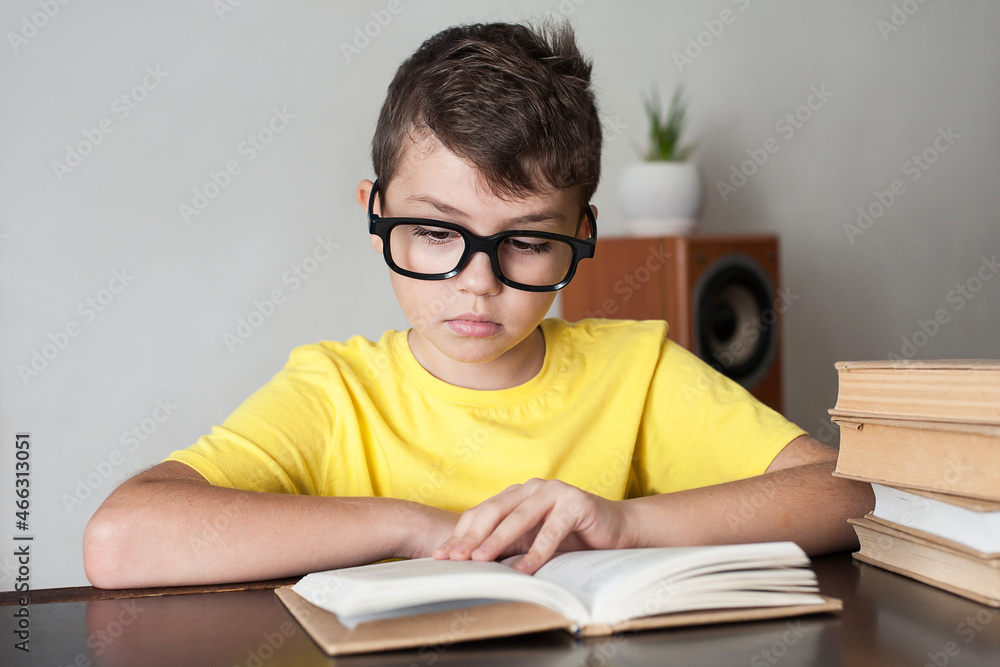 a boy with glasses and a yellow T-shirt reads books at the table at home. Home education a boy with glasses and a yellow T-shirt reads books at the table at home. Home education