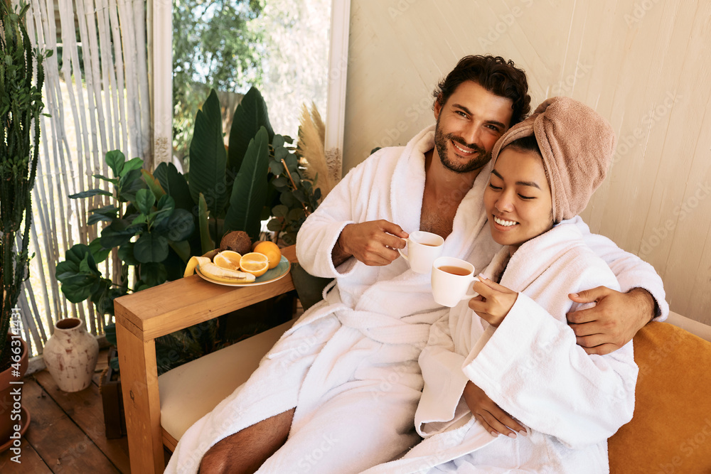 Loving young couple in white bathrobes spending time at spa and enjoying wellness tea. Couple while romantic weekend Loving young couple in white bathrobes spending time at spa and enjoying wellness tea. Couple while romantic weekend