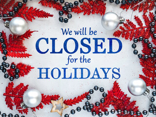 Signboard with the inscription We will be closed for the holidays and green branches of a Christmas tree. View from above, closeup, indoors, no people. Congratulations for family, friends, colleagues