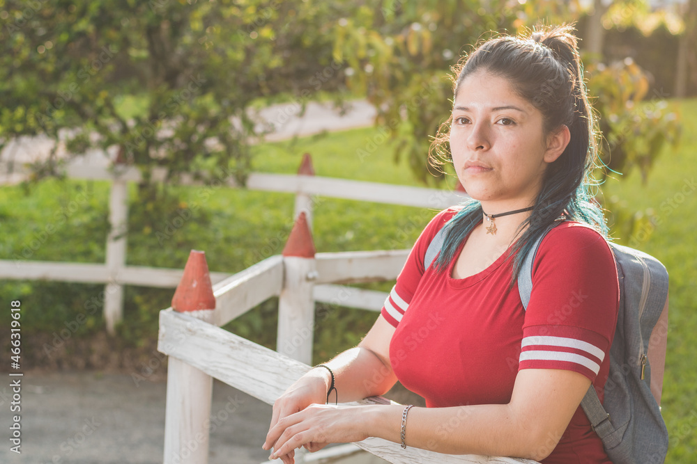 Beautiful young Latina college girl, waiting for her package next to a wooden fence, dressed in red and dyed blue hair, with a beautiful sunset in the background and a car driving away. Beautiful young Latina college girl, waiting for her package next to a wooden fence, dressed in red and dyed blue hair, with a beautiful sunset in the background and a car driving away.
