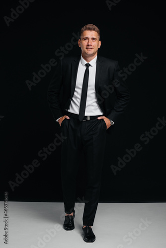 A handsome young man in a stylish black suit poses on a black background. A stylish business man. A big businessman.