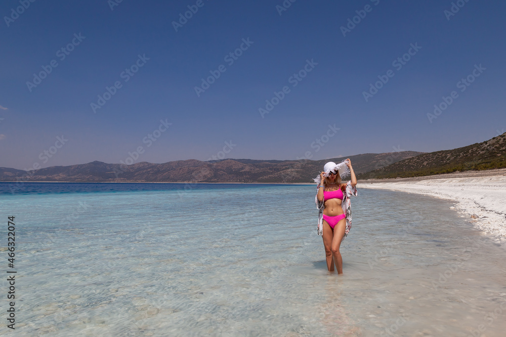 Happy beach body woman with sun hat on travel vacation on Salda Lake, Turkey. Slim legs sexy bikini girl sun tanning feeling free. Banner panorama with copy space on blue ocean background.