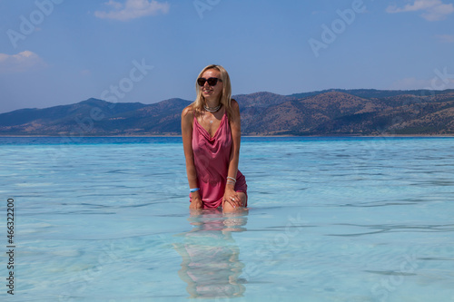 Young caucasian woman in the sunglasses and pink dress standing sexy posing in the Lake Salda, Turkey. Beautiful female happy relax walking on beach near sea with white sand and very clean blue water