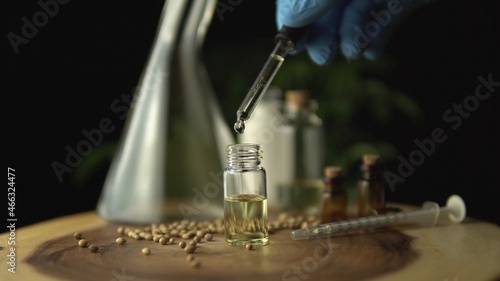 Macro close up of droplet pipette dosing biological and ecological oil of the hemp plant. Pharmaceutical herbal cbd oil in the small jar on the wood circle tree ring table. Organic pharma concept.