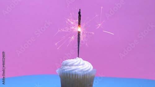 Cute and tasty vanilla coconut cupcake with burning sparklers on pink background. Close-up shot of bright burning Bengal fire in muffin dessert. Christmas and New Year mood. Shallow depth of field.