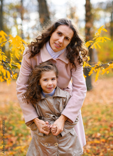Portrait of a mother and daughter in an autumn park. Happy people pose against the background of beautiful yellow trees. They hug and are happy together.