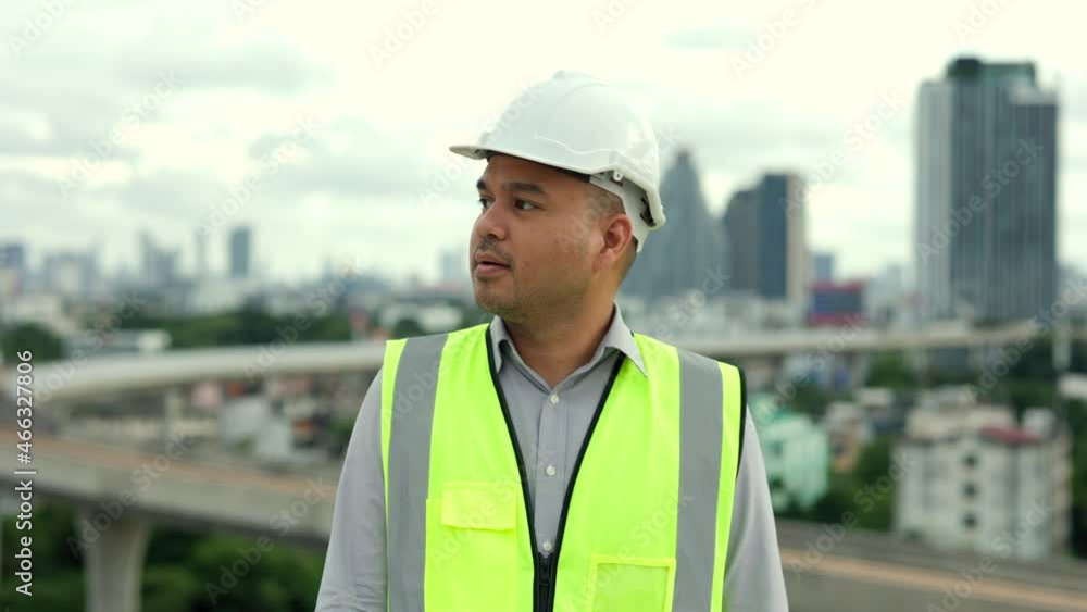 Asian engineer handsome man or architect looking forward with white safety helmet in city construction site . Standing on rooftop building construction at capital. Architect asian man working Asian engineer handsome man or architect looking forward with white safety helmet in city construction site . Standing on rooftop building construction at capital. Architect asian man working