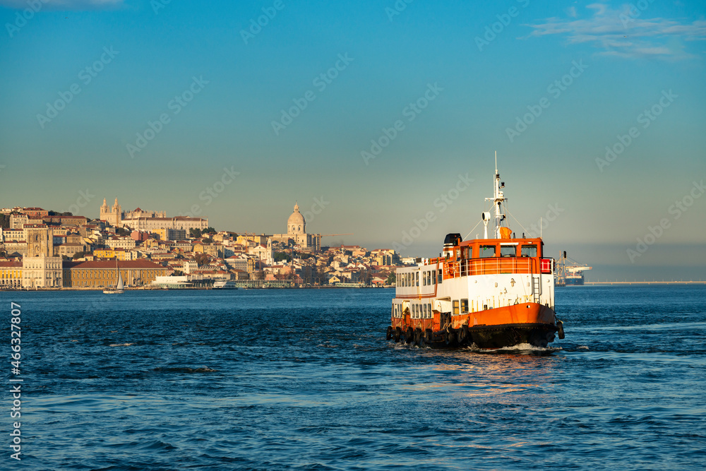Fototapeta premium A traditional cacilheiro ferry boat crossing the Tagus River (Rio Tejo) with the city of Lisbon skyline on the background, in Portugal