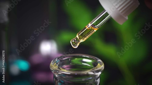 CBD Hemp oil, Hand holding droplet of Cannabis oil against blurry beaker background. Alternative Medicine. droplet dosing a biological and ecological hemp plant herbal pharmaceutical cbd oil.	
